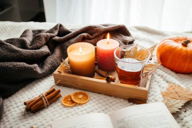 Sonbahar havası. Sıcak bir fincan çayla mum yakmak ve sıcak bir yatak örtüsünün üzerinde açık bir kitap. Konforlu ev dekorasyonu.