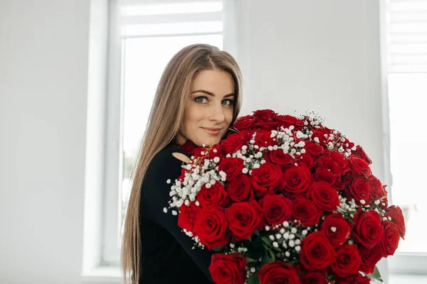 Kocaman bir buket gülle güzel, uzun saçlı kız gülümseyip kameraya bakıyor. Çiçekler her bayram için bir hediye ve çiçek teslimatıdır. Sevgililer Günü