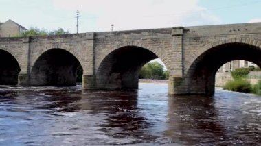 İngiltere 'nin Leeds, Batı Yorkshire' daki İngiliz kasabası Wetherby 'deki nehir kıyısından geçen eski güzel bir köprü, sıcak bir yaz gününde köye giden taş tuğla köprüyü gösteriyor.