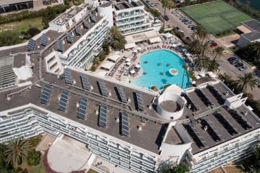 İspanya 'nın güzel Mayorka adasında çekilen hava aracı fotoğrafı çatıda güneş panelleri ve yazın açık yüzme havuzu olan bir otel binasının üst katını gösteriyor.