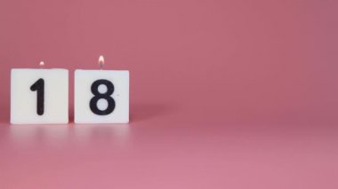 18 numaranın bir doğum gününü veya yıldönümünü kutlayan pembe bir arka planda yanıp söndüğünü söyleyen kare bir mum.