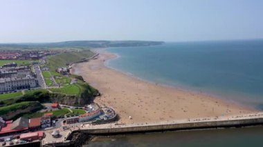 Kuzey Yorkshire, İngiltere 'deki güzel sahil ve Whitby kasabasının hava görüntüleri sıcak bir yaz gününde kumsalda dinlenen ve oynayan insanların insansız hava aracı görüntülerini gösteriyor.