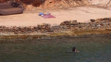 İspanya 'nın İbiza kasabasında plajda dinlenen kadın model, Santa Eularia des Riu kasabasında eşyaları ve havlusuyla birlikte okyanusta yüzen modeli gösteriyor.