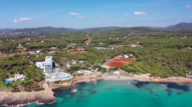 İspanya 'nın Balear adalarındaki güzel İbiza adasının, Playa Es Canar köyündeki sahil ve otelleri ve arkadaki manzaralı dağları gösteren hava görüntüleri.