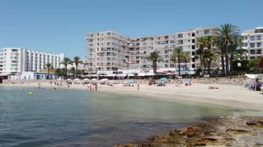 Santa Eularia des Riu 'daki Akdeniz kıyısındaki İbiza kasabasında Playa De Santa Eulalia olarak bilinen güzel plajda dinlenen insanların görüntüleri.