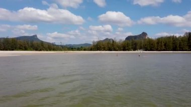 A beautiful beach scene taken at the Ao Nang Beach in Krabi, Thailand, showing people on the sandy beach in the ocean on the sand having fun in the sun on vacation