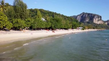 A beautiful beach scene taken at the Ao Nang Beach in Krabi, Thailand, showing people on the sandy beach in the ocean on the sand having fun in the sun on vacation
