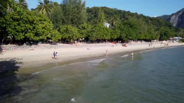 A beautiful beach scene taken at the Ao Nang Beach in Krabi, Thailand, showing people on the sandy beach in the ocean on the sand having fun in the sun on vacation