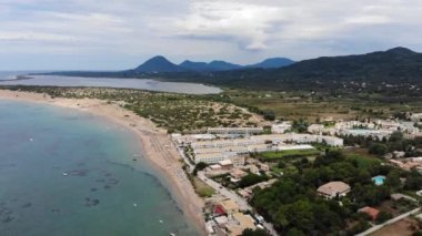 Aerial footage of the beautiful small town known as St George South, Greek city of Corfu Greece, showing people relaxing on the beach with hotels and mountains in the background on the Issos Beach