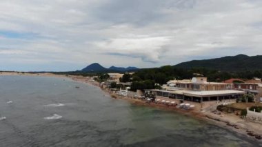 Aerial footage of the beautiful small town known as St George South, Greek city of Corfu in Greece, showing the Issos Beach and restaurants with mountains in the background