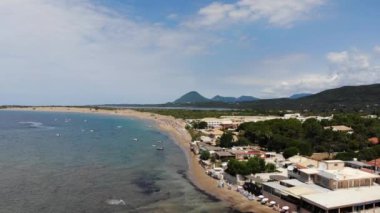 Aerial footage of the beautiful small town known as St George South, Greek city of Corfu Greece, showing people relaxing on the beach with hotels and mountains in the background on the Issos Beach