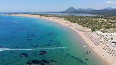 Aerial footage of the beautiful small town known as St George South, Greek city of Corfu Greece, showing people relaxing on the Issos beach corfu with hotels and mountains in the background