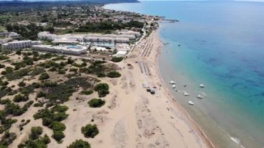 Aerial footage of the beautiful small town known as St George South, Greek city of Corfu Greece, showing people relaxing on the beach with hotels and mountains in the background on the Issos Beach