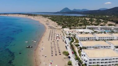 Aerial footage of the beautiful small town known as St George South, Greek city of Corfu Greece, showing people relaxing on the beach with hotels and mountains in the background on the Issos Beach