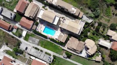 Aerial footage of the beautiful small town known as St George South in the city of Corfu Greece, showing people relaxing and having fun in a hotel swimming pool with people relaxing and having fun