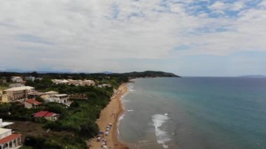 Aerial footage of the beautiful small town known as St George South in the city of Corfu Greece, showing people relaxing and having fun on the sunny Agios Georgios Beach with parasols