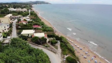 Aerial footage at beautiful small town of St George South in the city of Corfu Greece, showing people relaxing on the beautiful beach and coast on a bright sunny summers day at Agios Georgios Beach