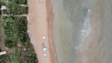 Aerial straight down top view of the village of St George South in Corfu showing the beautiful ocean with holiday makers relaxing and sunbathing on the Agios Georgios Beach in the summer time