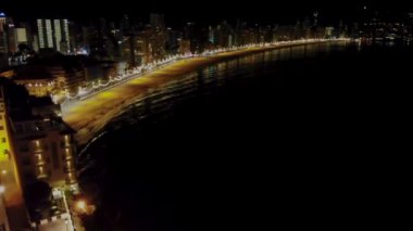 Aerial night time footage of the Spanish town of Benidorm showing the bright lights on the coast and coastal area beach taken in the evening showing the bright lights of Benidorm on the promenade.