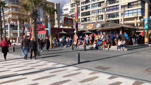 明るい晴れた日にビーチバーの反対側のメインストリップでスペインのベニドームを歩く人々 — ストック動画