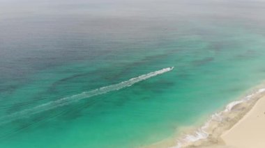 Aerial footage of the beautiful beach and coastline of Cape Verde (Capo Verde) showing a speed boat speeding on the water and waves crashing in to the goldren sandy beach.