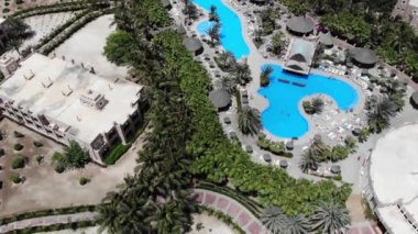 Aerial footage of the Hotel Riu Palace Cabo Verde Cape Verde showing the swimming pools and holiday makers relaxing and sunbathing in the sun next to the swimming pools on a beautiful sunny day