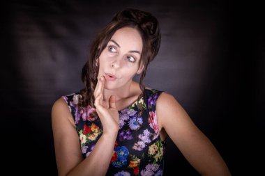 Uzun kahverengi kumral saçlı, siyah arka planda çiçekli bir elbise giyen çekici, zayıf bir kadın model.