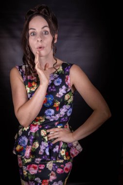 Uzun kahverengi kumral saçlı, siyah arka planda çiçekli bir elbise giyen çekici, zayıf bir kadın model.