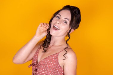 Sarı ya da turuncu arka planda uzun kahverengi kumral saçlı çekici bir kadın model. Eski moda noktalı bir elbise giyiyor. Gülümsüyor ve mutlu görünüyor.