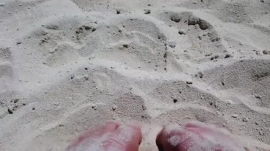 Güneşli bir günde, tropikal kumsalda kumla oynayan insanların ayakları okyanus kıyısında tatil yapan beyaz adamların ayak ve ayak parmaklarını gösteriyor..