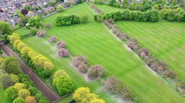 Aerial drone view footage of the beautiful blossom trees in the spring time filmed in the town of Harrogate, North Yorkshire UK showing the trees and freshly cut grass in the British town.
