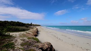 Küba 'nın Varadero plajının önündeki güzel sahil güneşli bir yaz gününde dalgaları ve temiz okyanus sularını gösteriyor ve bir çift kumsalda romantik bir yürüyüş yapıyor.