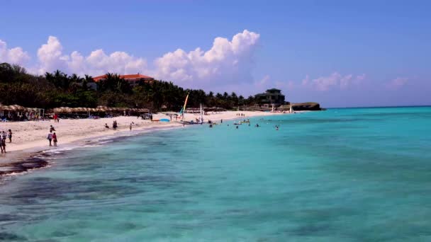 キューバのバラデロにあるキューバビーチの美しいビーチフロントは 8Kの品質で撮影されたビーチでリラックスして楽しんでいる人々と波ときれいな海の水を示しています — ストック動画