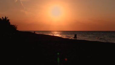 Küba 'nın Varadero kentindeki kumsalın güzel bir görüntüsü sahilin kıyısında, kumlu sahilde romantik bir çiftin sahil boyunca yürüdüğü deniz dalgalarıyla batan güzel güneşi gösteriyor..
