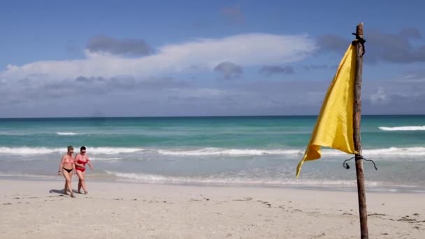 2022年3月22日キューバのバラデロ キューバのバラデロにあるキューバビーチの美しいビーチフロントビーチでは 風に黄色の旗が吹いており 2人の女性がビーチを歩いています — ストック動画