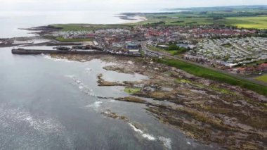 Aerial footage of the seaside coastal town of the village of Seahouses, a large village on the North Northumberland coast in England, showing the harbour and coastal front in the summer time.