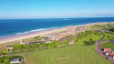 Aerial footage the famous Bamburgh Castle, a castle on the northeast coast of England, by the village of Bamburgh in Northumberland showing a drone view of the castle and sandy beach in the summer.