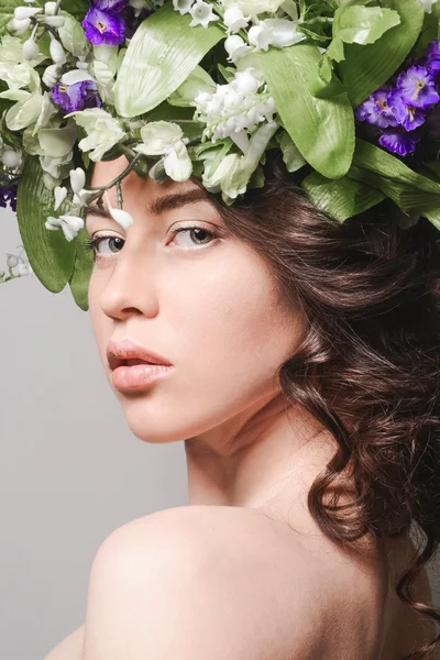 Skönhet porträtt av en ung flicka med blommor i håret på grå studio bakgrund Stock Snímky