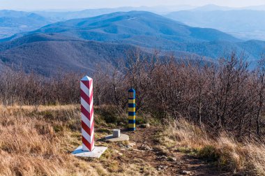 Border markes on a Polish-Ukraine boundary. The Polish eastern border, is also the border of the European Union and NATO. In the background, the blue sky and trees, bushes and grass of Bieszczady Mountains National Park, Poland
