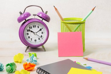 Masanın üzerinde bir çalar saat, bir not defteri ve boş bir pembe not kağıdı var. Okul eğitimi veya iş geliştirme kavramı.