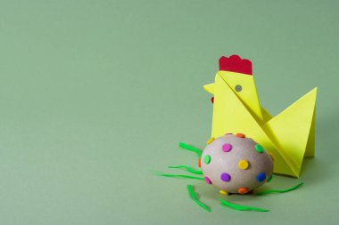Şirin sarı origami tavuğu ve yeşil arka planda yaratıcı paskalya yumurtası. Paskalya konsepti.