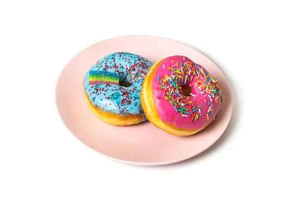 Due ciambelle multicolori con un arcobaleno si trovano su un piatto rosa su uno sfondo bianco — Foto Stock