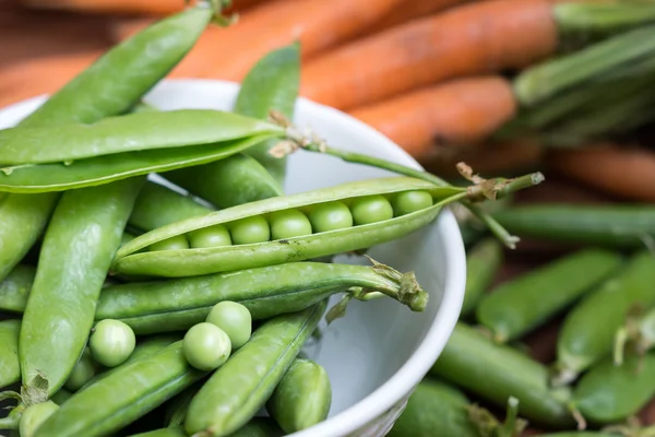 Ärt pods i en skål med morötter — Stockfoto