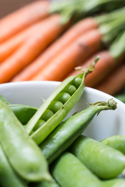 Ärt pods i en skål med morötter — Stockfoto