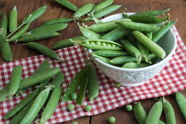 Erbsenschoten in einer Schüssel auf Holztisch — Stockfoto