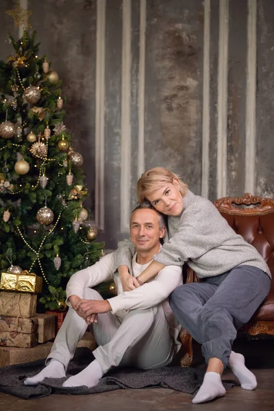 Güzel, yetişkin bir kadın ve bir adam bir koltuğa oturur ve bir Noel ağacının yanında sarılırlar. 