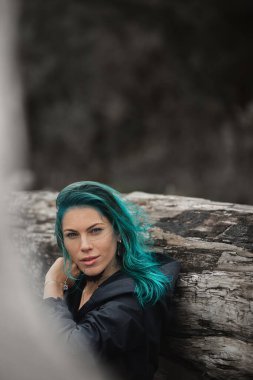 Güzel, mavi saçlı bir kadın kumsalda bir tahtada oturur.