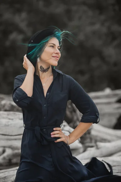 beautiful woman with blue hair and hat walks on the windy beach