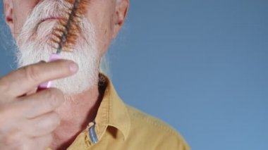 Yaşlı adam beyaz sakalını tarıyor. 