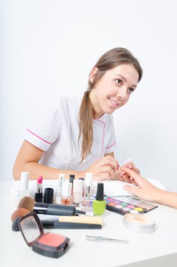 Bayan güzellik uzmanı, müvekkilinin manikür yaparken profesyonel kıyafetleri içinde giyinmiş. masada kozmetik çok. fırça, boya, ruj, Far, ruj.